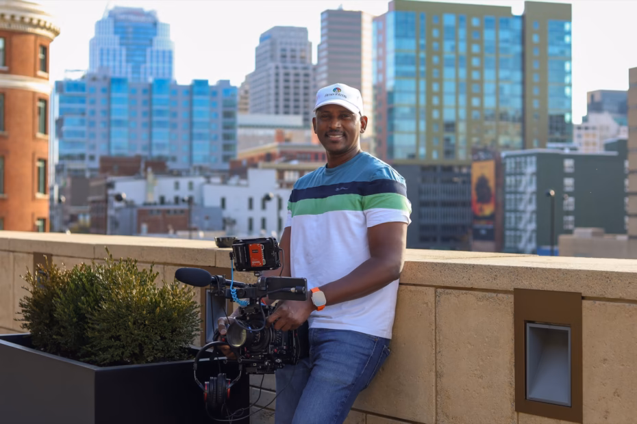 Souley Oumarou, founder of AmeriFilms, holding a cinema camera on a rooftop with the city skyline behind him